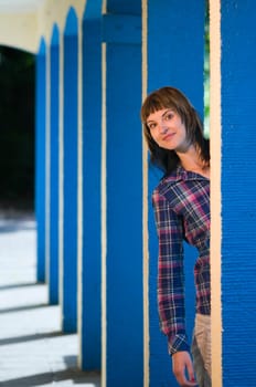 Upper body portrait of a young brunette woman posing between blue architectural pillars