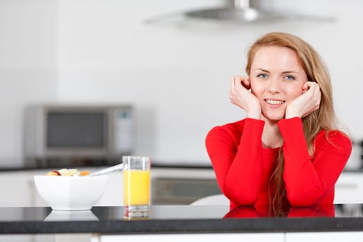 Young woman enjoying a bowl of fresh fruit in her kitchen with orange juice