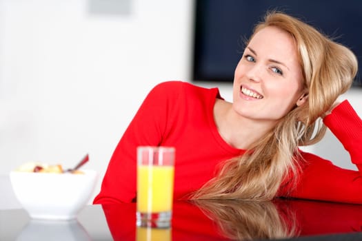 Young woman enjoying a bowl of fresh fruit in her kitchen with orange juice