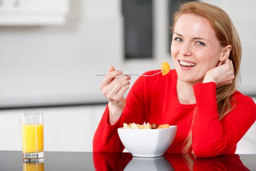 Young woman enjoying a bowl of fresh fruit in her kitchen with orange juice
