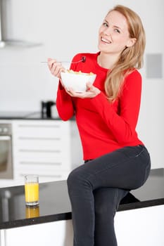 Young woman enjoying a bowl of fresh fruit in her kitchen with orange juice