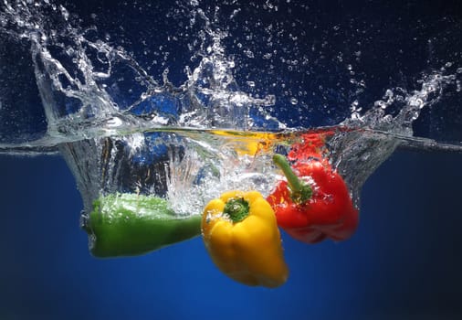Three peppers falling into water  Blue background