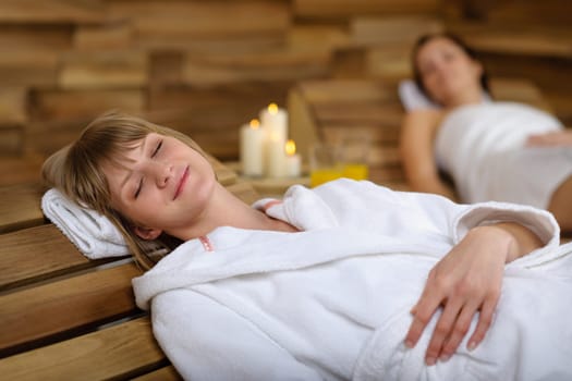 Happy young woman relaxing on wooden chair at luxury spa