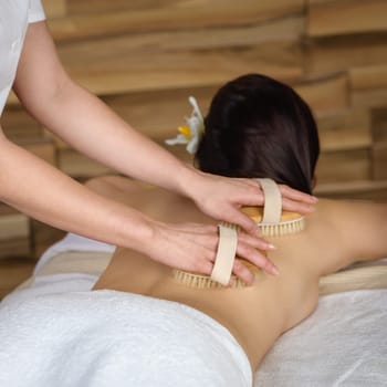 Beautiful brunette having wooden brush massage at luxury spa