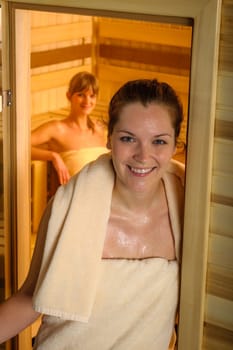 Two young sweaty woman wrapped in towels at sauna room