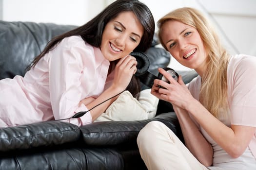 Two young woman listening to music on headphones at home.