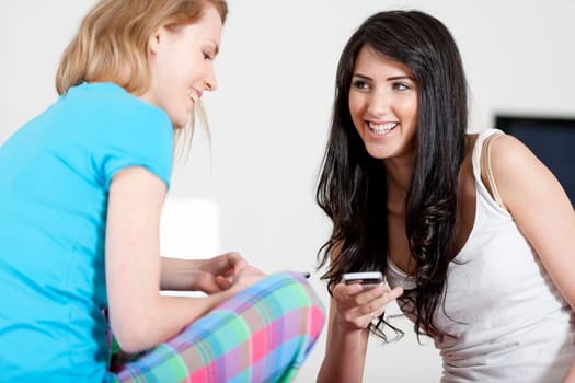 Two young woman chatting and using their mobile phones at home