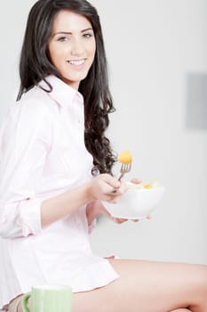 Young woman in underwear and pink shirt sat in kitchen eating breakfast