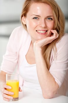 Young woman in pink shirt sitting at dining table at home with orange juice