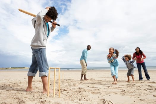 Family playing cricket on beach