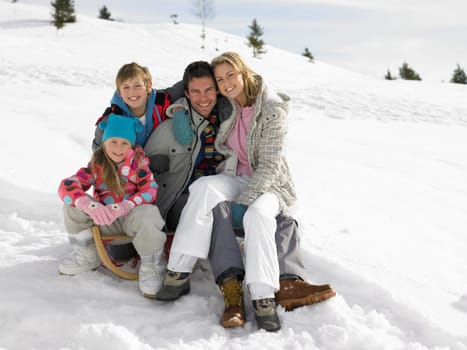 Young Family Sitting On A Sled In The Snow