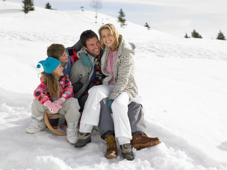 Young Family Sitting On A Sled In The Snow