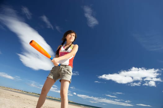 Teenage girl playing baseball on beach