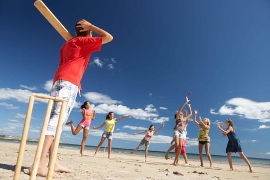 Teenagers playing cricket on beach