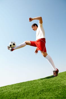 Portrait of soccer player kicking ball on football field