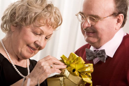 Image of aged woman opening giftbox with her husband near by