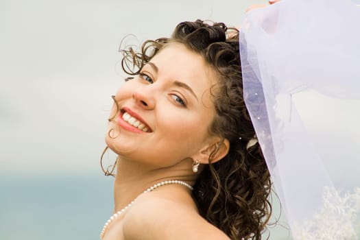 Image of happy young bride touching wedding veil and looking at camera