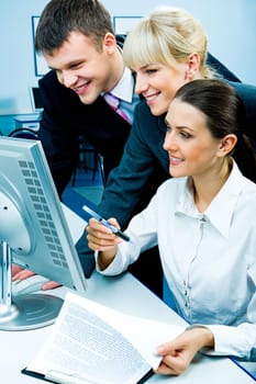 Businessteam of three smiling people looking at the monitor in the computer room