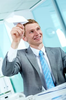 Portrait of a successful employer at workplace holding paper plane