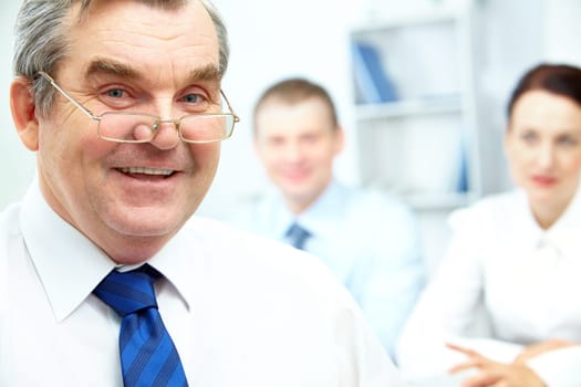 Face of senior businessman looking at camera with two partners on background