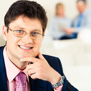 Portrait of successful businessman touching his chin and looking at camera with smile in working environment