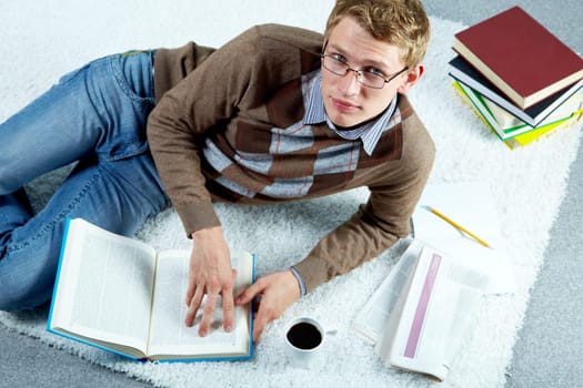 Image of serious student lying on the floor and reading book