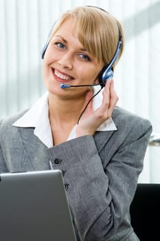 Portrait of beautiful smiling blond businesswoman in gray suit holding a pen in her hand and touching headset