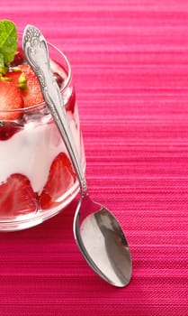 Individual serving of a gourmet strawberry dessert with layered cream alternating with fresh fruit and pudding in a glass container with copspace