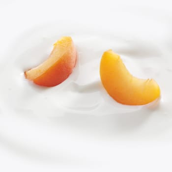 Fresh cut peach slices lay lightly on a fresh serving of yogurt