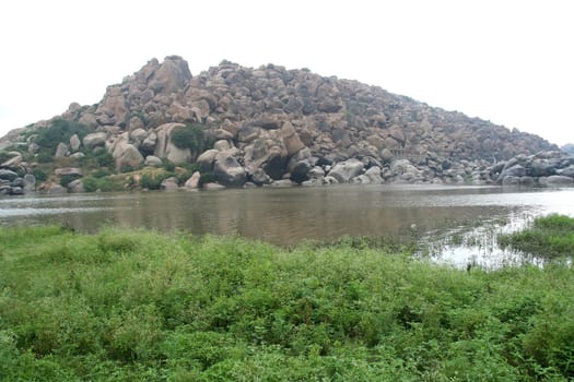 View of Tungabhadra River and rocky hill with grass foreground at Hampi, Karnataka, India, Asia