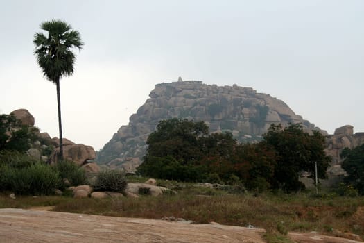 View of trees and rocky hill with temple atop at Hampi, Karnataka, India, Asia