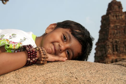 Girl child with ornamental hand bands enjoying rocky lap at Vijayavithala temple in Hampi, Karnataka, India, Asia