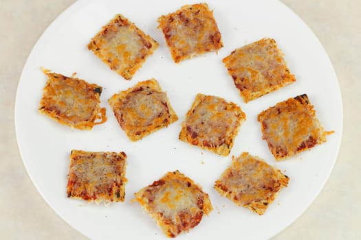 Ten square, broiled mini pizza snacks on a white plate.