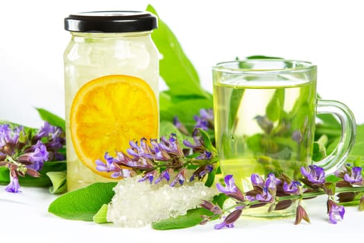 Glass of sweet herbal tea with flowering salvia and sage, sugar crystals and sliced orange, a medicinal remedy used in Auyurveda naturopathy