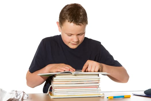 Teenager sitting reading at a table from a pile of books researching information for his homework assignment