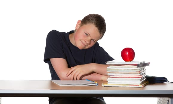Teenager sitting at his desk looking at the camera with a quizzical expression with pile of books and a healthy ripe red apple