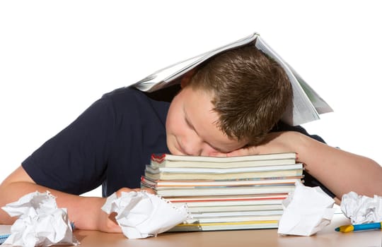 Tired out by studying for exams a young teenage boy has fallen asleep with his head resting on his textbooks and crumpled paper lying scattered around him