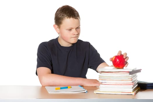 Teenager contemplating a ripe red apple balanced on top of his textbooks as he sits at his desk