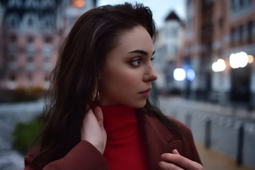 Dramatic close up portrait of young beautiful woman looking aside against evening city background