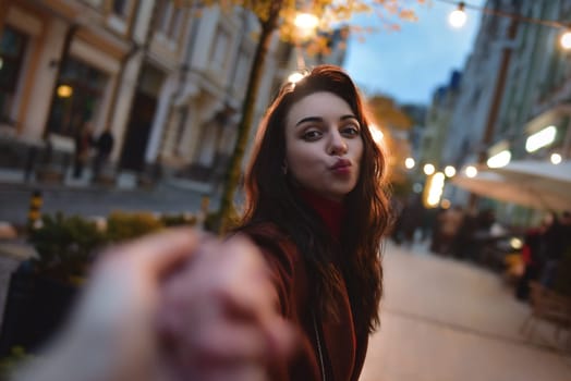 follow me. Beautiful romantic girl in red coat takes her boyfriend's hands while walking in the evening city