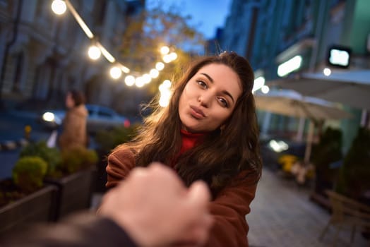 follow me. Beautiful romantic girl in red coat takes her boyfriend's hands while walking in the evening city