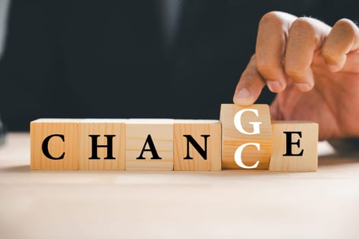 Hand of adult man flips wood block, revealing CHANCE from CHANGE. Success, strategy, and positive mindset illustrated. Vintage table adds depth. Change is showcased.