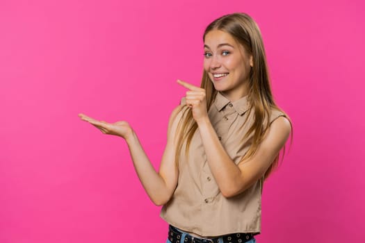 Young woman showing thumbs up and pointing left empty place, advertising area for commercial text, copy space for goods promotion advertisement. Girl isolated on pink studio background. Lifestyles