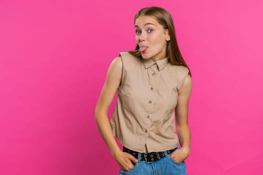 Cheerful funny young woman showing tongue making faces at camera, fooling around, joking, aping with silly face, teasing, bullying, abuse. Girl isolated alone on pink studio background. Lifestyles
