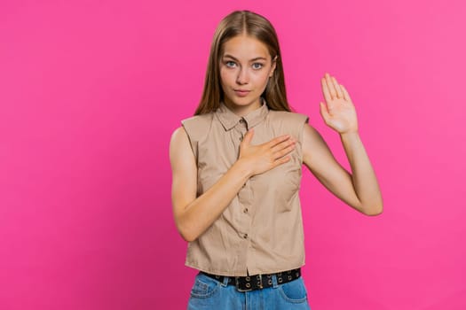 I swear to be honest. Sincere responsible young woman raising hand to take oath, promising to be honest and to tell truth, keeping hand on chest. Girl isolated on pink studio background. Lifestyles