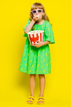 Excited young cute school girl in 3D glasses eating popcorn, watching interesting tv serial, sport game, film, online social media movie content. Teen female child kid on yellow background. Vertical