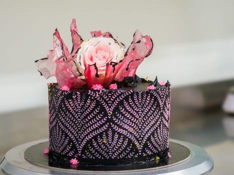 frosted icing black decorate cake for birthday celebration, real rose topping and pink sweet swirls in professional kitchen