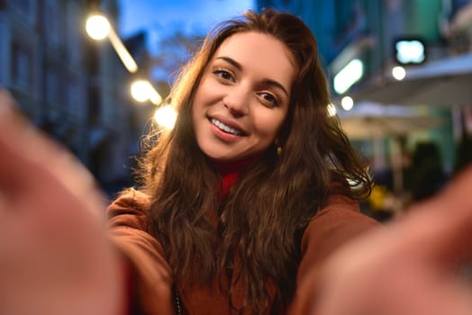 Happy elegant young woman in red coat taking selfies while walking around the city. woman hugs her boyfriend