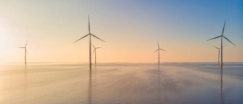 Windmill park in the ocean at sunset, drone aerial view of windmill turbines generating green energy, windmills isolated at sea in the Netherlands.