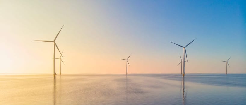 Windmill park in the ocean, drone aerial view of windmill turbines generating green energy, windmills isolated at sea in the Netherlands at sunset